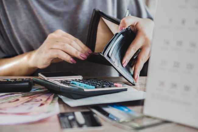 kvinna öppnar tom plånbok vid bord med miniräknare, pengar och kreditkort